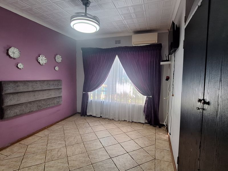 A spacious bedroom featuring tiled flooring, a built-in cupboard, a ceiling fan, and a wall-mounted air conditioning unit.