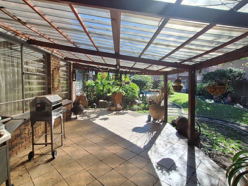 Covered outdoor patio area featuring tiled flooring, a timber pergola structure with translucent roofing, and direct access to the rear garden.