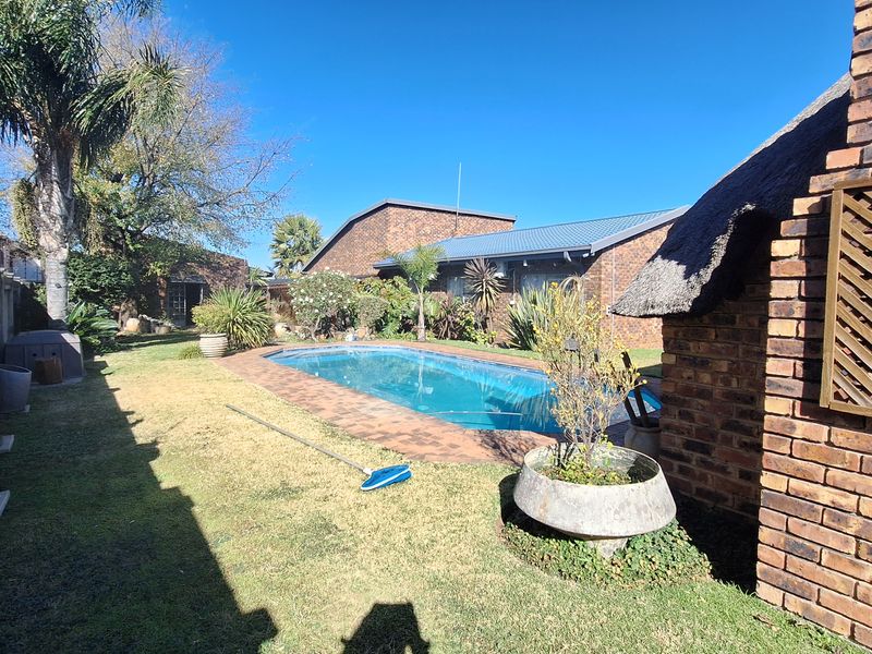 A private backyard featuring a swimming pool with brick paving, surrounded by a landscaped garden and a traditional thatched-roof structure.