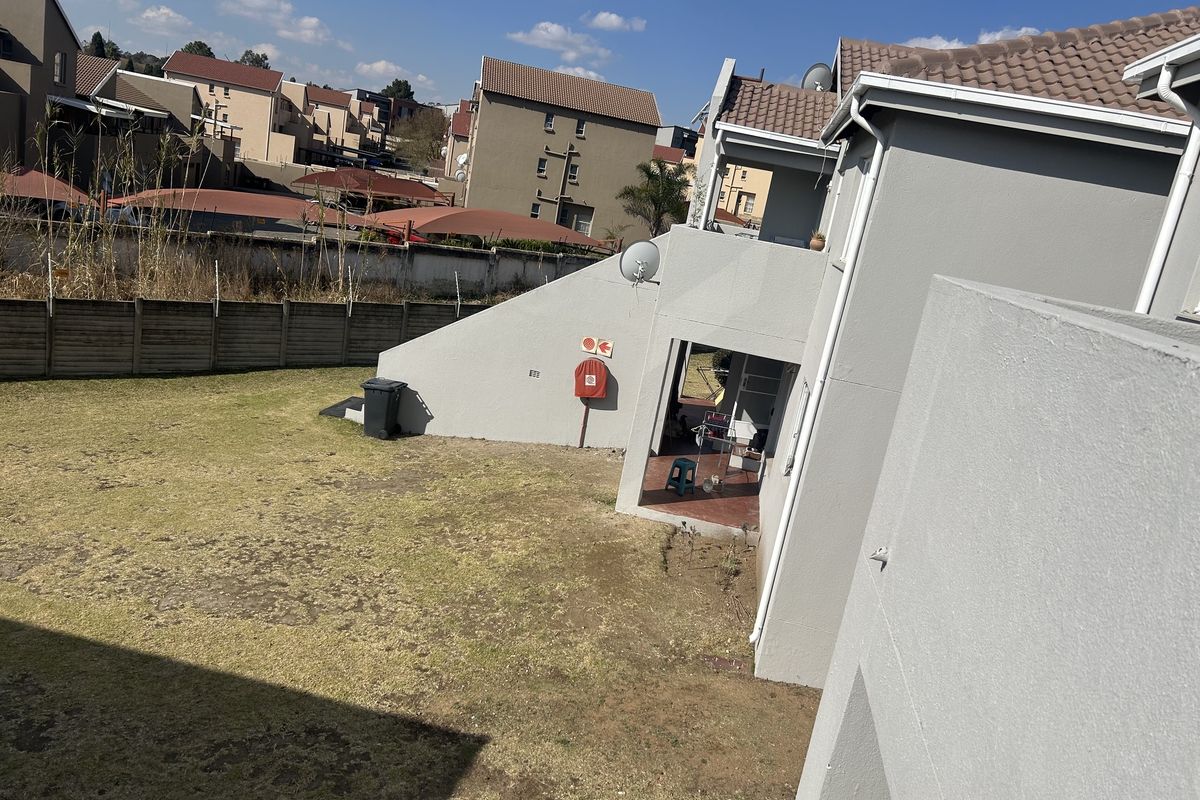 Rear view of the townhouse showing a private garden area, tiled roof, and exterior wall with a mounted fire hose reel.