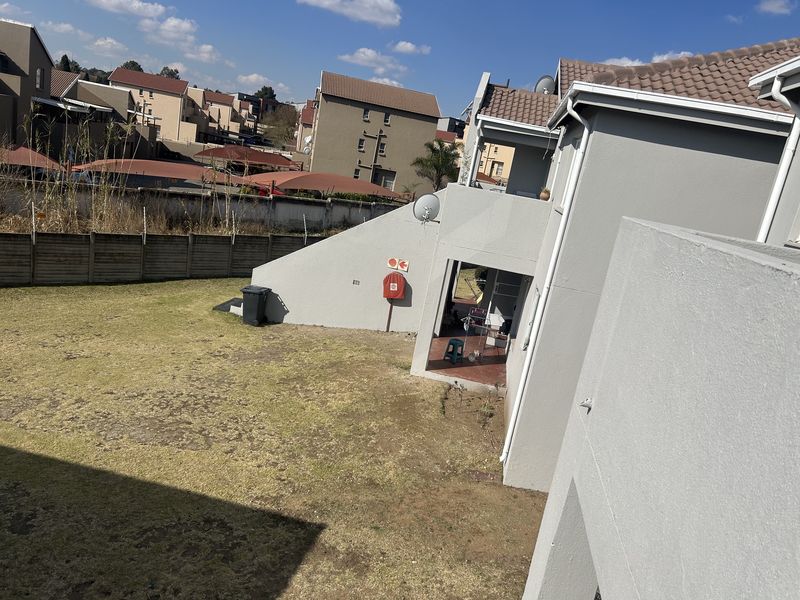 Rear view of the townhouse showing a private garden area, tiled roof, and exterior wall with a mounted fire hose reel.