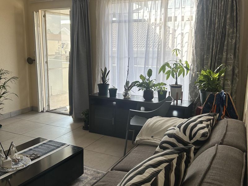 A bright living room featuring tiled flooring and direct access to an outdoor balcony through a sliding door, offering natural light.