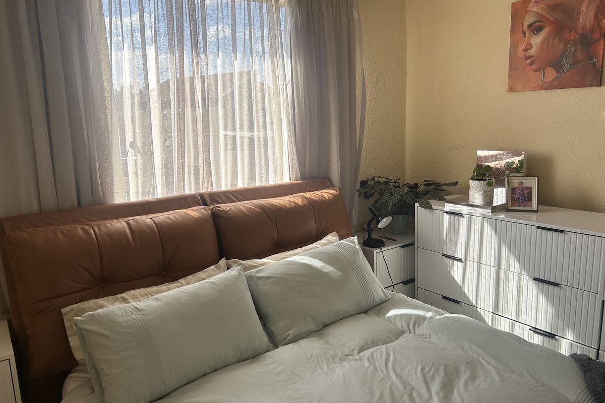 A sunlit bedroom featuring a large window with sheer curtains, providing natural light to the space.