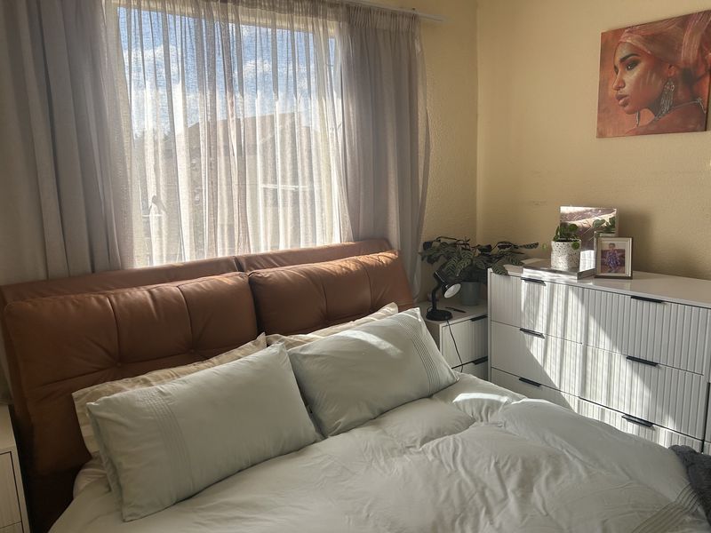 A sunlit bedroom featuring a large window with sheer curtains, providing natural light to the space.