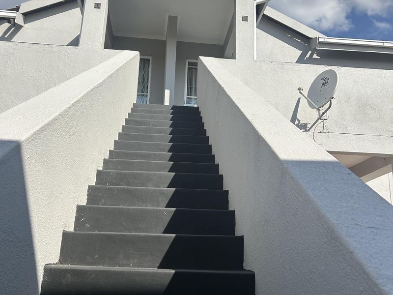 Exterior view of a townhouse entrance featuring a prominent staircase leading to the upper level with a mounted satellite dish.