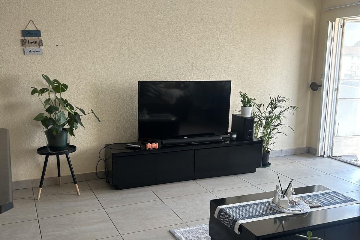 A living room featuring neutral tiled flooring and a sliding glass door providing access to the exterior.