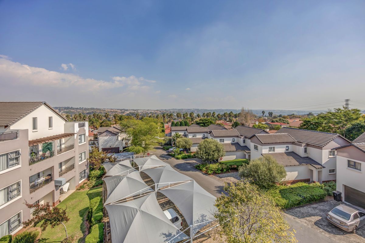 An elevated aerial view of a residential apartment complex featuring paved driveways, shade cloth carports, and well-maintained landscaped grounds.