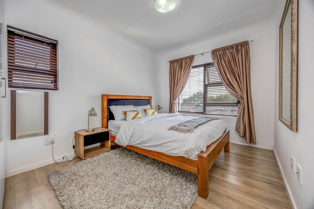 A well-maintained bedroom featuring light-toned laminate flooring, dual window treatments with venetian blinds and curtains, and neutral wall finishes.