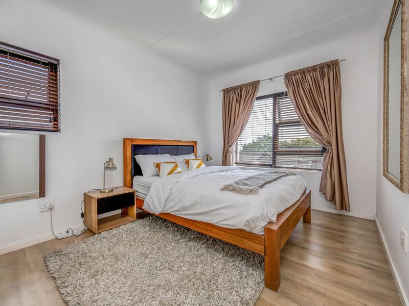 A well-maintained bedroom featuring light-toned laminate flooring, dual window treatments with venetian blinds and curtains, and neutral wall finishes.
