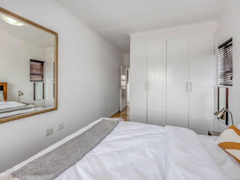 A well-maintained bedroom featuring built-in cupboards, neutral finishes, and natural light through venetian blinds.