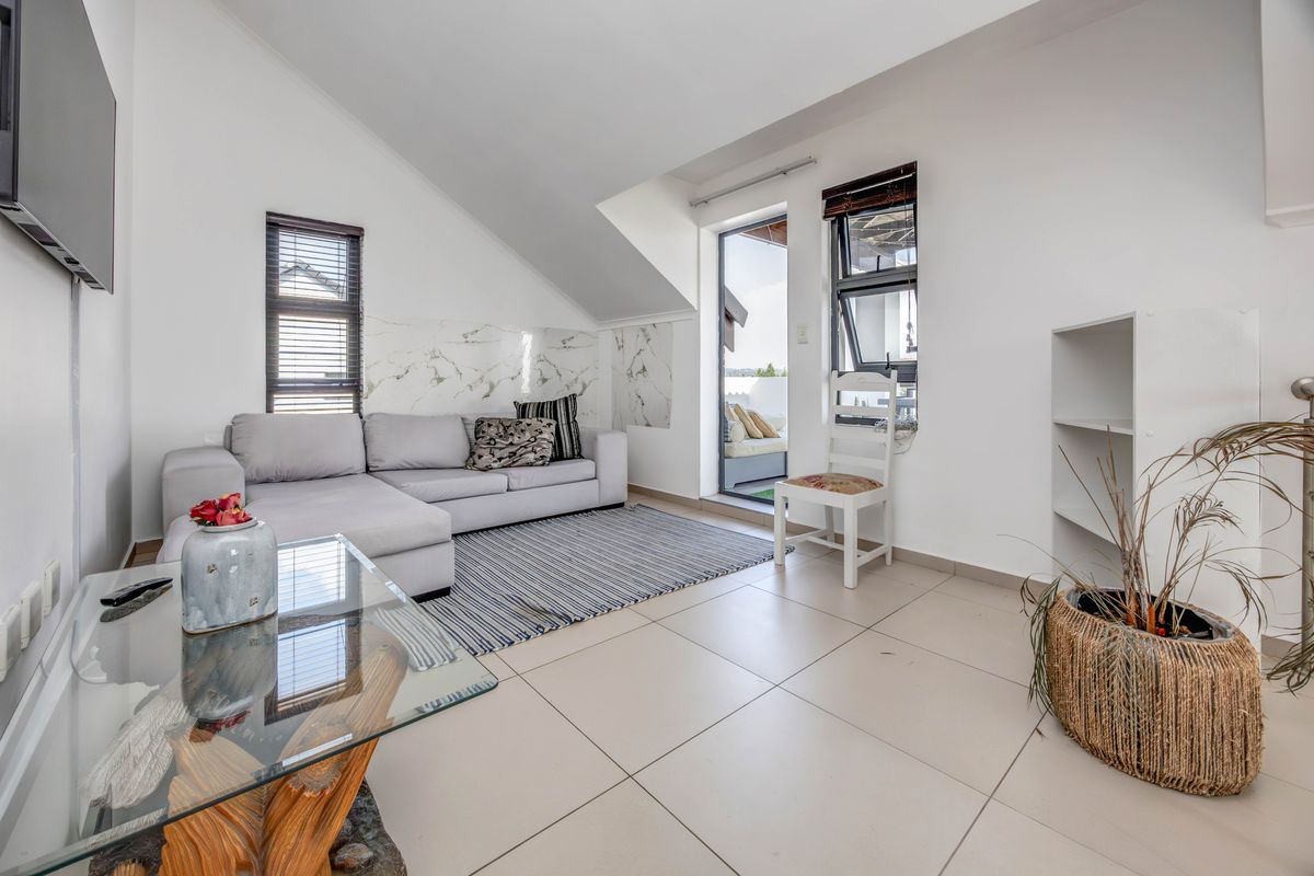 Bright living room featuring tiled floors, a sloped ceiling, marble-look wall accents, and direct access to an outdoor balcony area.