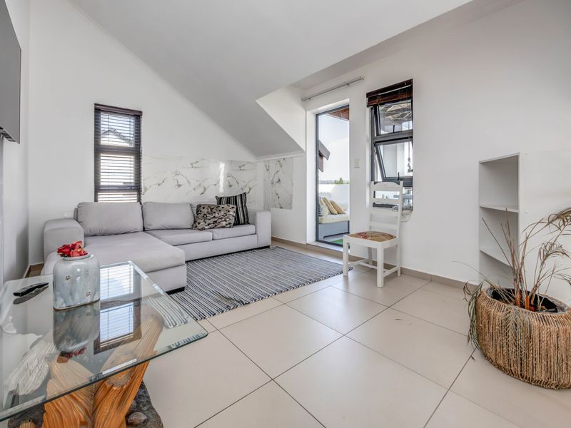 Bright living room featuring tiled floors, a sloped ceiling, marble-look wall accents, and direct access to an outdoor balcony area.