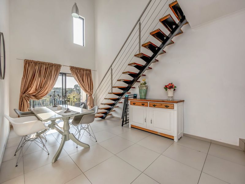 Spacious open-plan living and dining area featuring high ceilings, modern tiled flooring, and a striking architectural staircase with a metal balustrade.