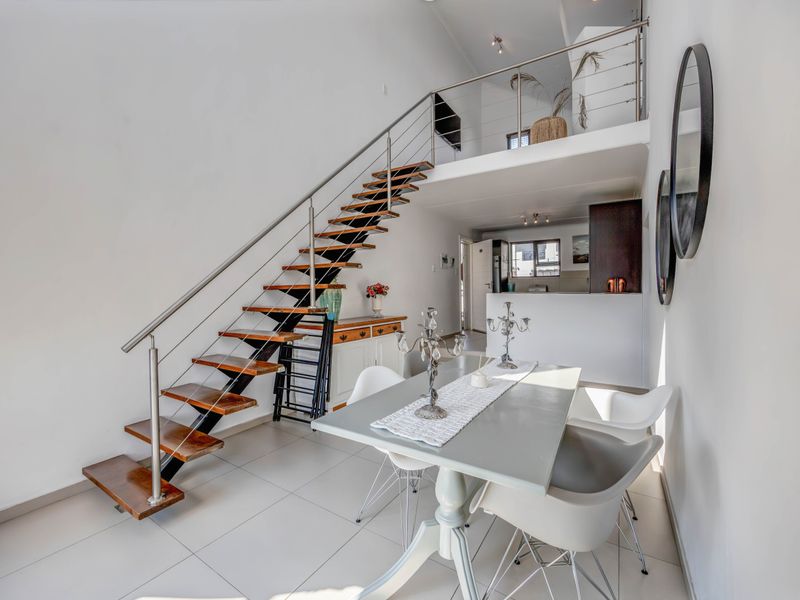 Open-plan living area featuring a modern staircase with timber treads, stainless steel balustrade, mezzanine level, and tiled flooring throughout.
