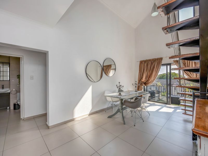 Open-plan living area featuring a striking spiral staircase, vaulted ceilings, large format floor tiles, and direct access to a balcony through sliding glass doors.