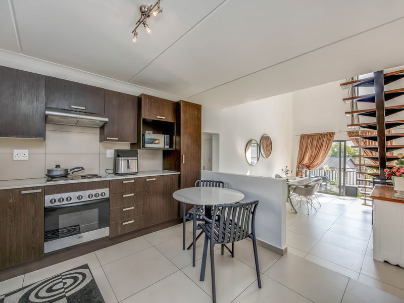 Open-plan kitchen and living area featuring dark wood cabinetry, built-in appliances, tiled flooring, and a distinctive spiral staircase leading to the upper level.