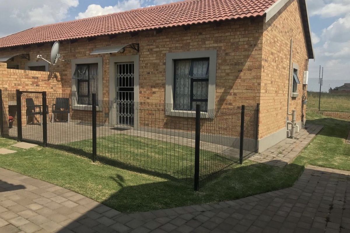 A well-maintained face brick apartment exterior featuring a private fenced garden, paved patio area, and secure entrance.