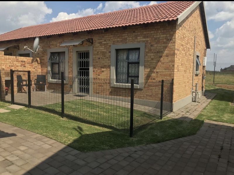 A well-maintained face brick apartment exterior featuring a private fenced garden, paved patio area, and secure entrance.