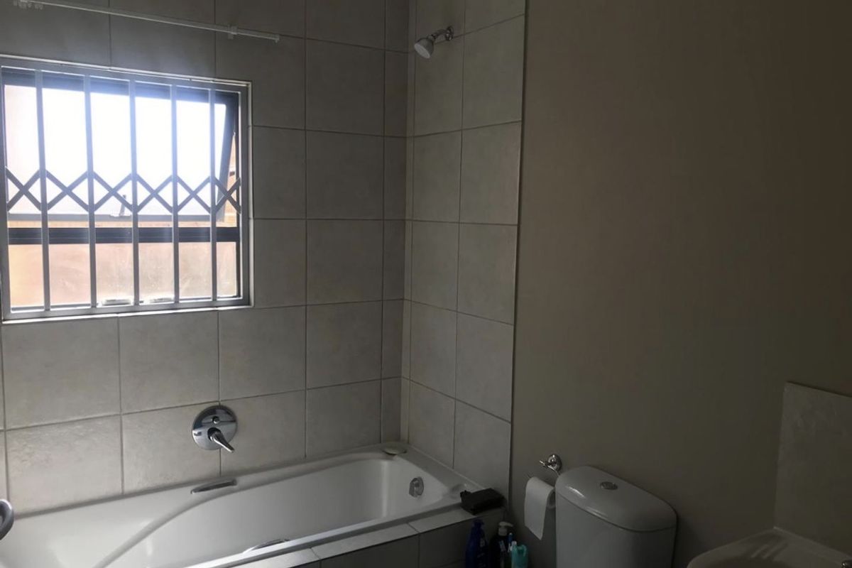 A functional bathroom featuring a bathtub with shower head, toilet, and basin, finished with neutral wall tiling and a window with security bars.