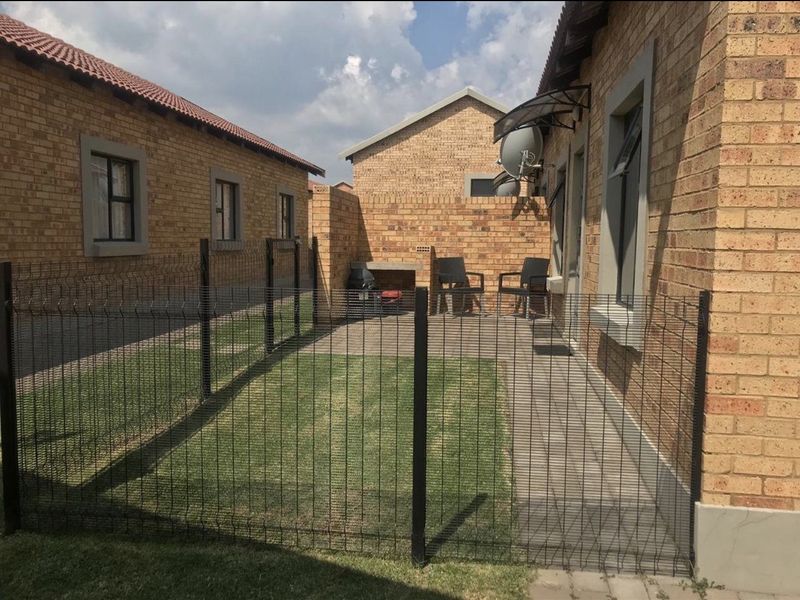 A private rear courtyard featuring a paved patio area, built-in braai, small lawn, and secure wire mesh fencing.