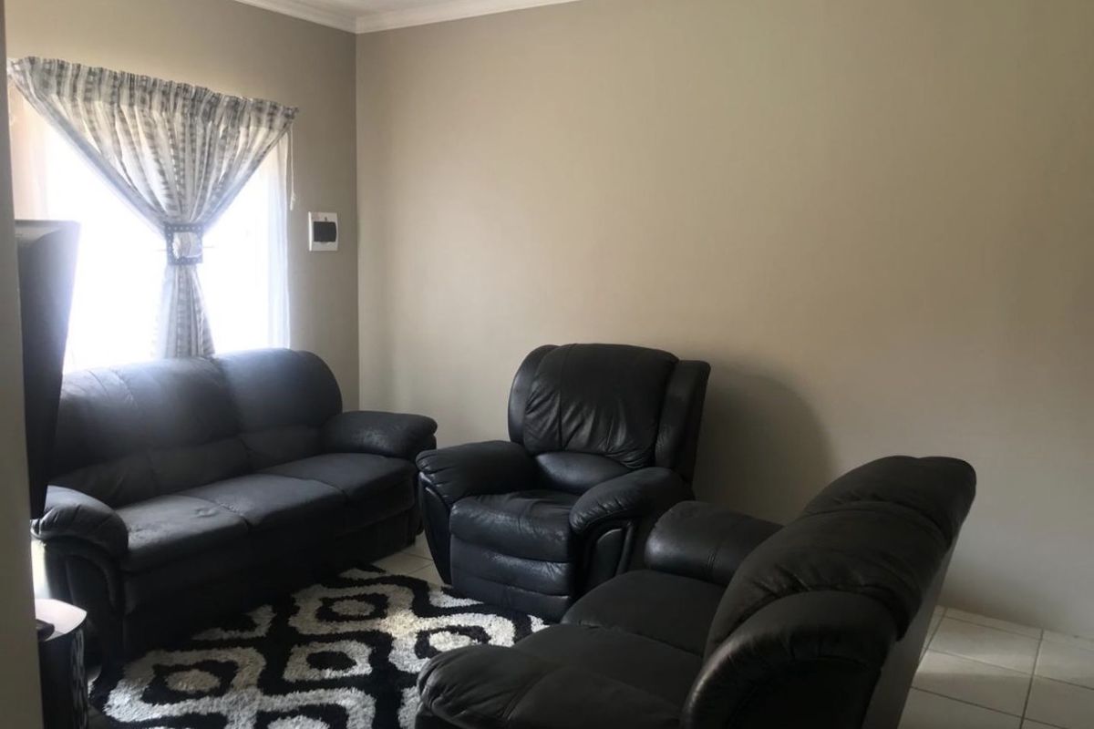 A living room featuring neutral wall paint, crown molding, and tiled flooring, providing a functional and well-maintained space.