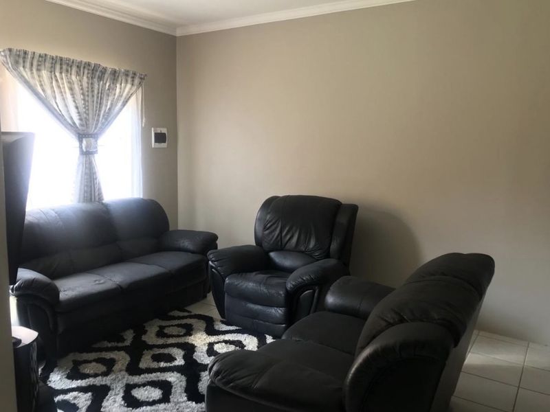A living room featuring neutral wall paint, crown molding, and tiled flooring, providing a functional and well-maintained space.