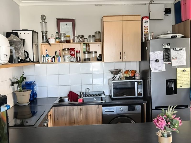 A functional kitchen featuring laminate countertops, tiled backsplash, built-in cabinetry, and integrated appliances including a washing machine and microwave.