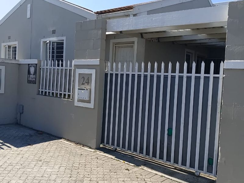 Front exterior view of the property featuring a paved driveway, secure metal gate, carport, and perimeter wall with security features.