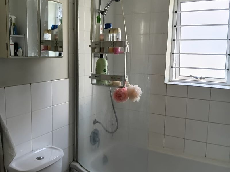 A functional bathroom featuring a bathtub with a shower screen, a toilet, a vanity unit, and a medicine cabinet.