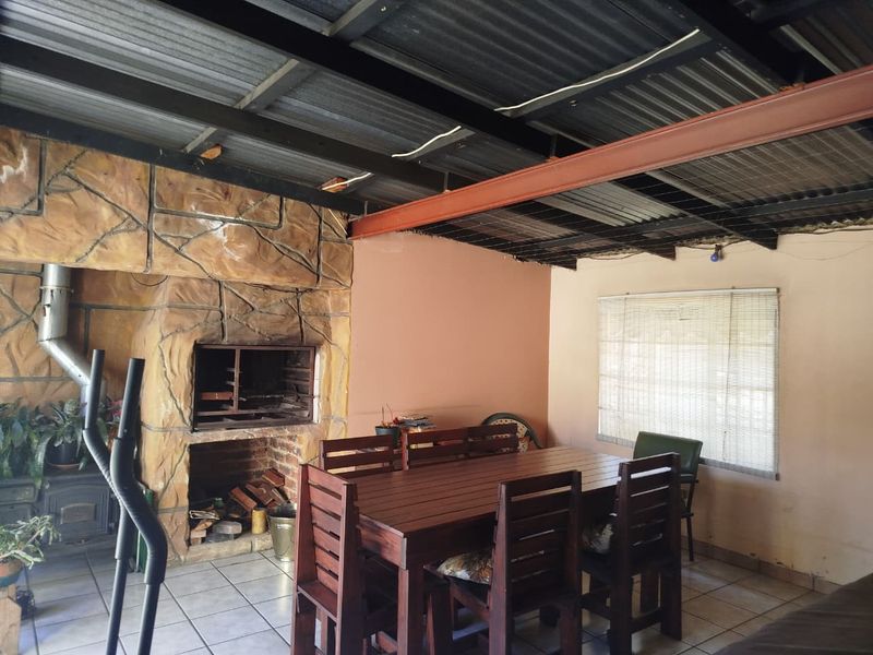 Covered patio area featuring a built-in braai with stone cladding, exposed steel roof structure, and tiled flooring, suitable for outdoor entertaining.