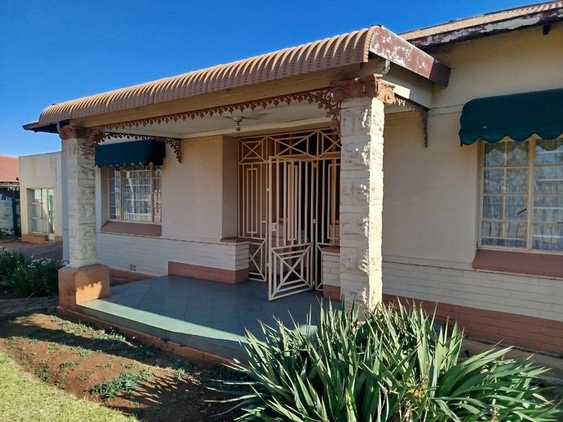 Front facade of a house featuring a covered porch with stone pillars, decorative metal detailing, and security gate access.