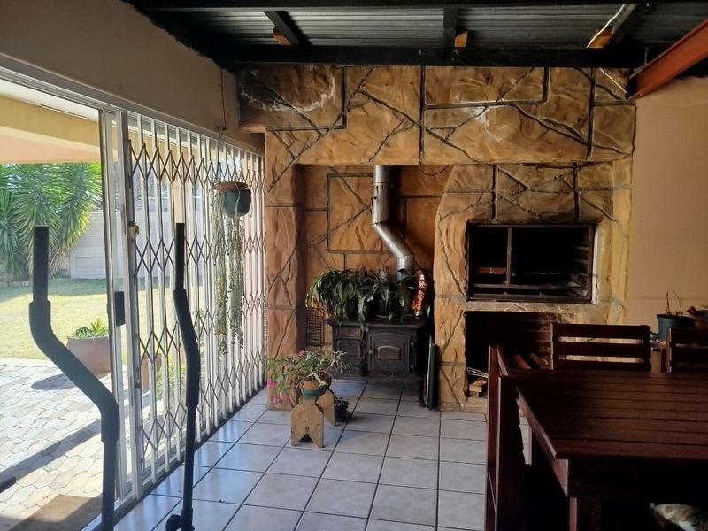 Covered patio area featuring a built-in braai, fireplace, tiled flooring, and direct access to the garden through a security gate.