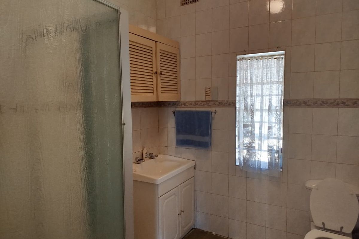 A functional bathroom featuring a shower enclosure, vanity basin, wall-mounted storage, and toilet, finished with classic wall tiling.