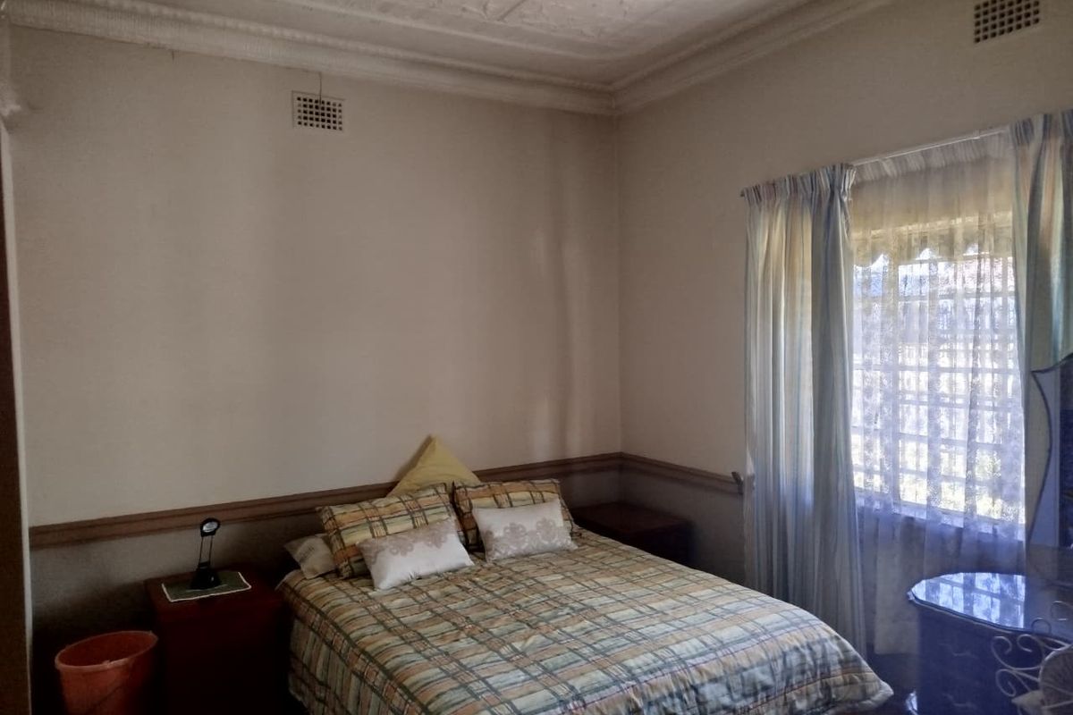 A bedroom featuring a classic pressed metal ceiling, chair rail molding, and a window fitted with security bars.