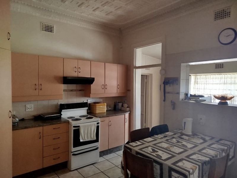 A dated kitchen featuring original laminate cabinetry, a freestanding stove, and a unique pressed metal ceiling with a convenient pass-through window to the dining area.