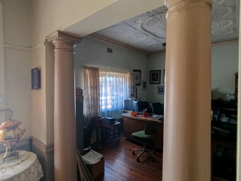A home office space featuring original decorative ceiling details, timber flooring, and prominent structural columns framing the entrance.