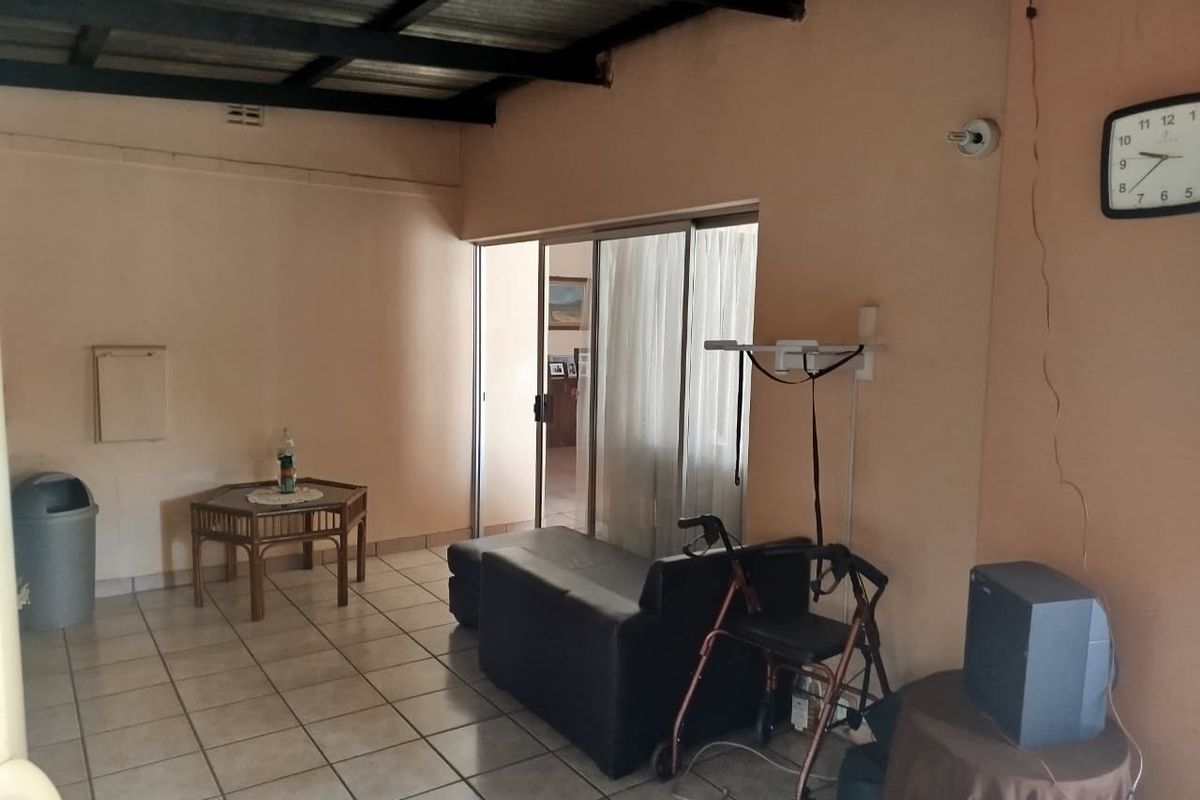 A living area featuring ceramic floor tiles, an exposed beam ceiling, and a sliding glass door leading to an adjacent space.