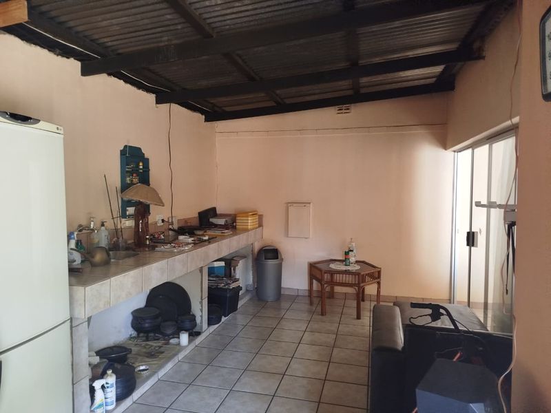 A functional kitchen area featuring tiled countertops, a built-in sink, and tiled flooring, with direct access to an outdoor space via sliding glass doors.