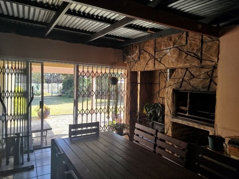 Covered patio area featuring a built-in braai, tiled flooring, and sliding glass doors providing direct access to the rear garden.