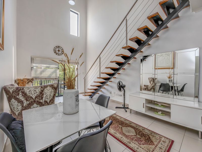 Spacious living area featuring high ceilings, tiled flooring, and a modern open-tread staircase with a stainless steel balustrade leading to the upper level.