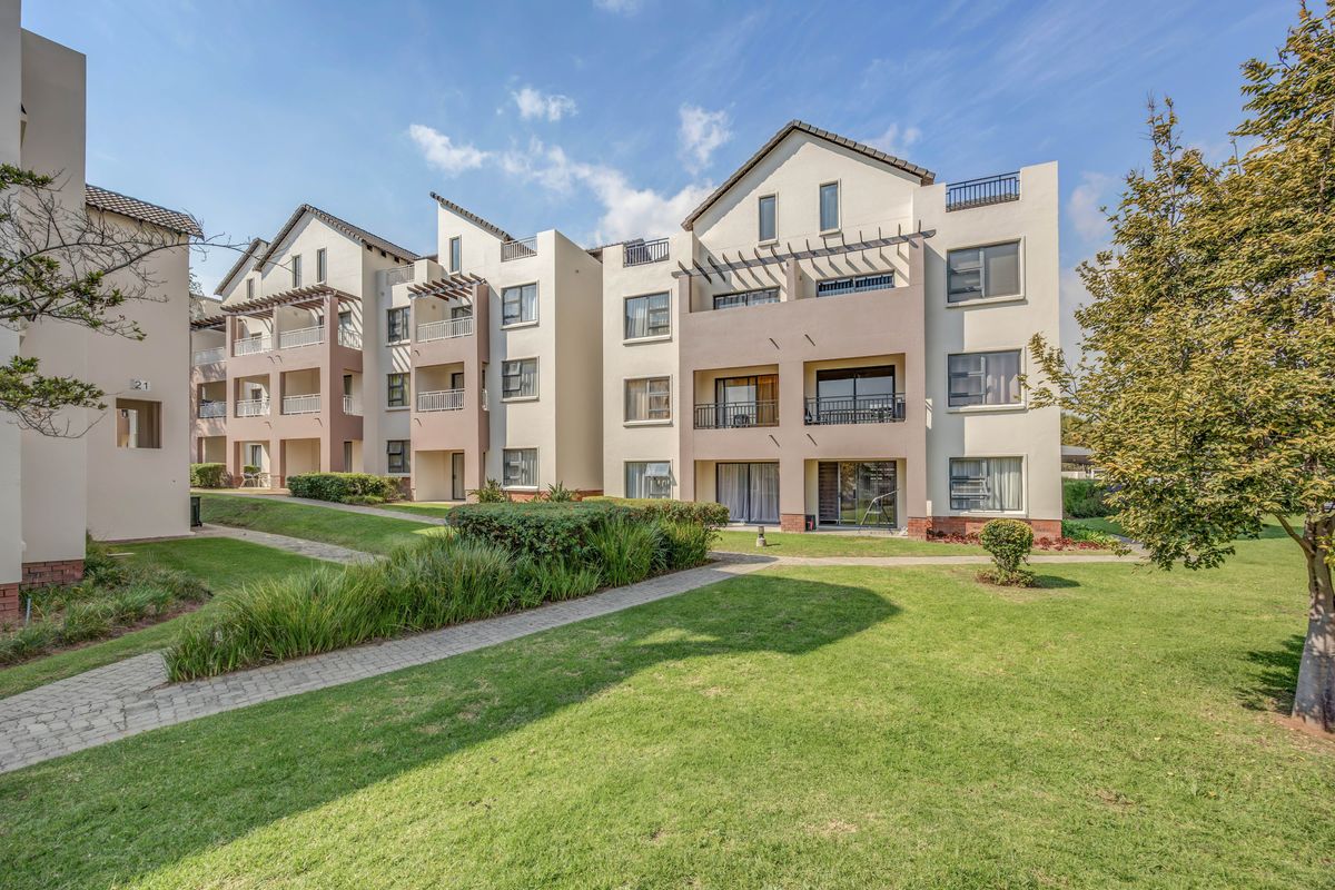 A view of the rear elevation of a modern apartment complex featuring balconies, landscaped gardens, and paved walkways.