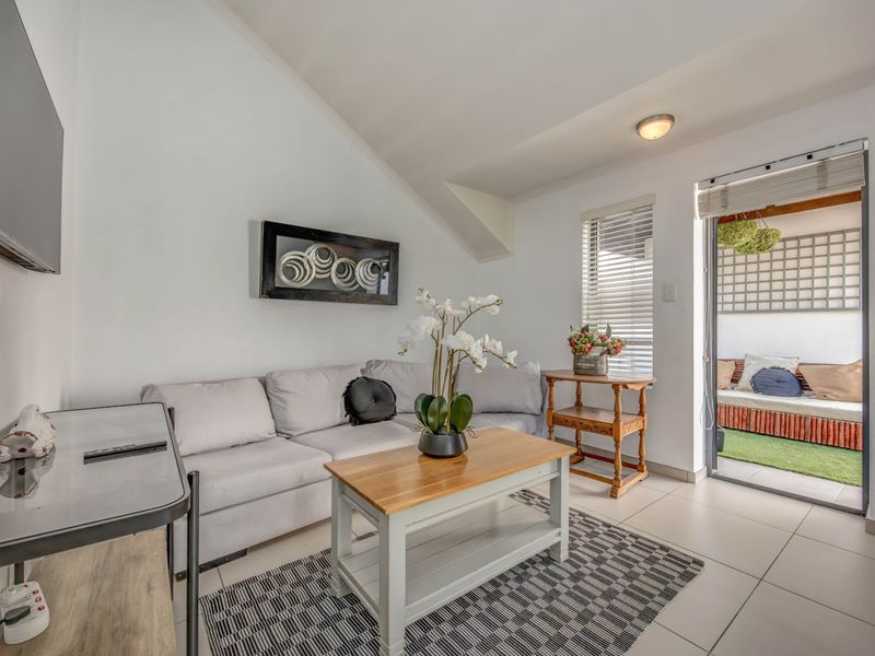 A bright living room featuring tiled flooring, a sloped ceiling, and direct access to an outdoor patio area through a sliding glass door.