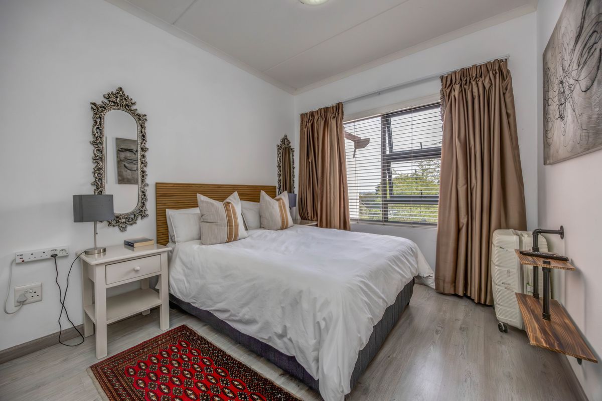 A well-lit bedroom featuring light-toned laminate flooring, neutral walls, and a window with fitted blinds, providing a comfortable and functional living space.