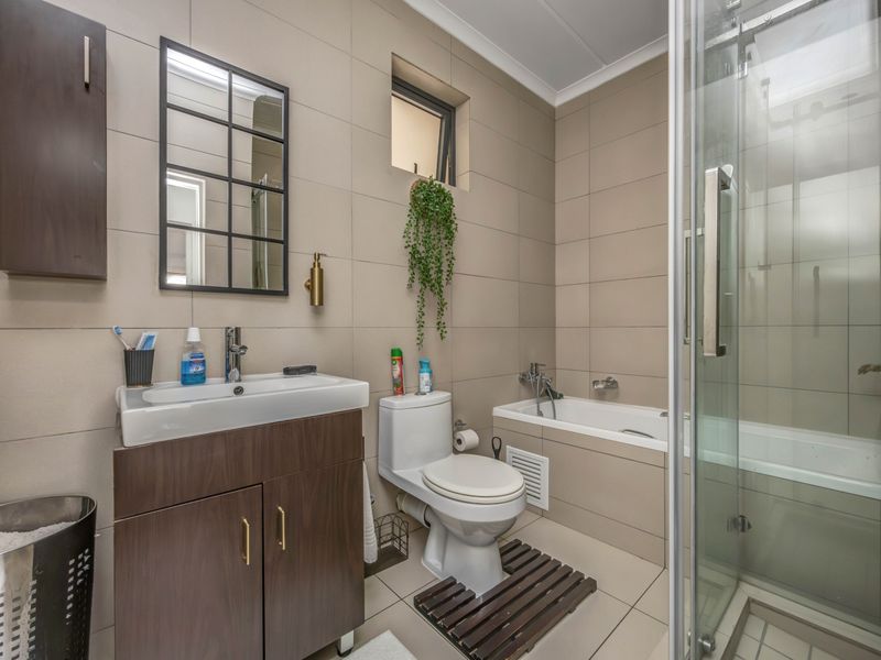 Modern bathroom featuring a vanity cabinet, ceramic basin, toilet, bathtub, and a separate glass-enclosed shower with neutral wall and floor tiling.
