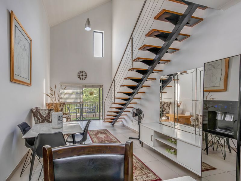 Spacious open-plan living area featuring a striking floating staircase, vaulted ceilings, and large sliding doors leading to a balcony, creating a bright, airy atmosphere.