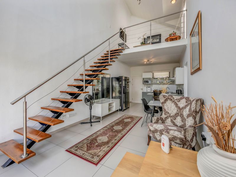 Open-plan living area featuring a modern floating staircase with stainless steel balustrades, leading to a mezzanine level, with an integrated kitchen space.