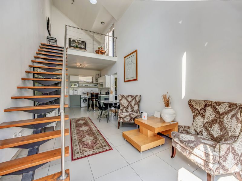 Open-plan living area featuring a modern staircase, mezzanine level, and integrated kitchen with tiled flooring and high vaulted ceilings.
