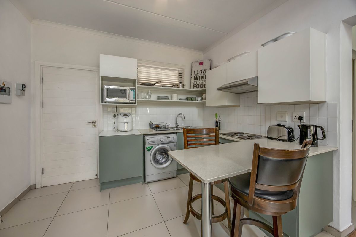 Compact kitchen featuring modern cabinetry, stone countertops, integrated laundry plumbing, and a breakfast bar, finished with neutral floor tiles and a tiled backsplash.