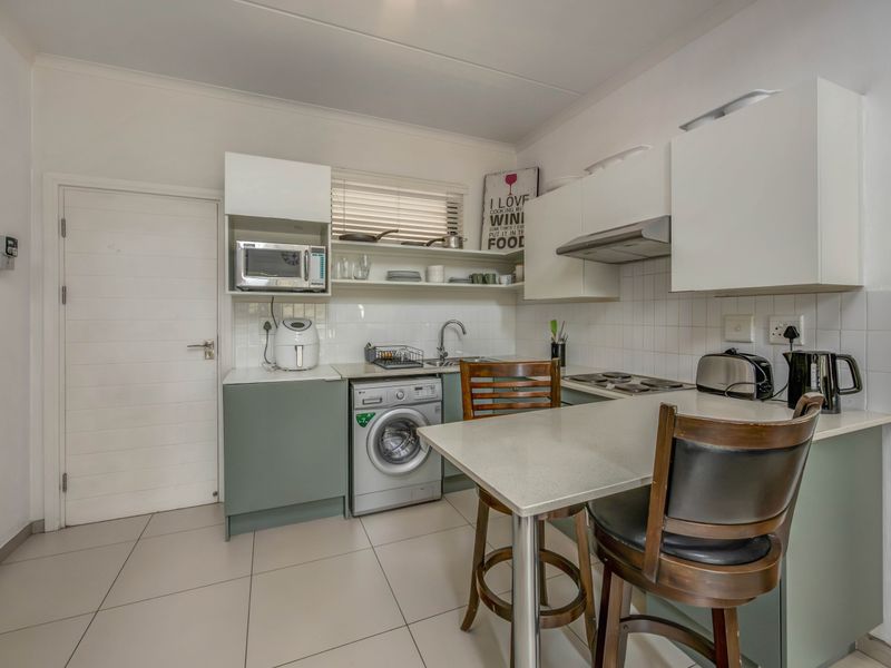 Compact kitchen featuring modern cabinetry, stone countertops, integrated laundry plumbing, and a breakfast bar, finished with neutral floor tiles and a tiled backsplash.
