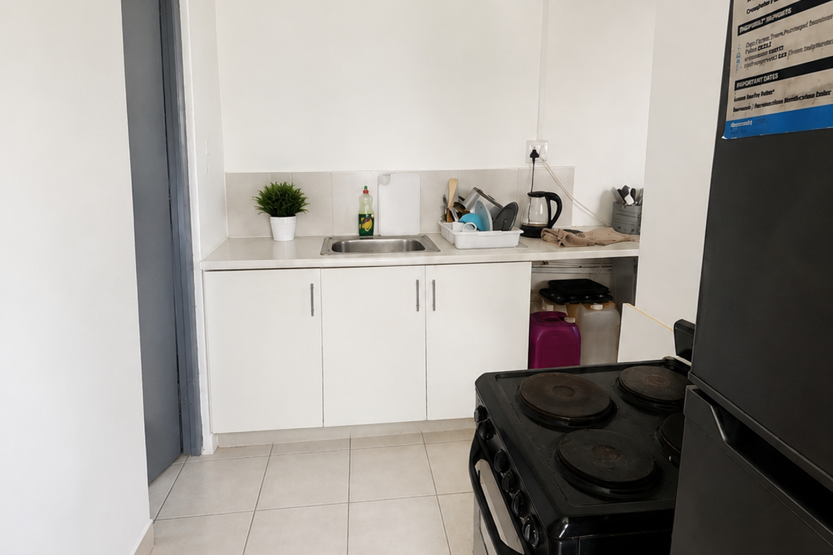 A compact kitchen area featuring white cabinetry, a stainless steel sink, tiled splashback, and ceramic floor tiles.